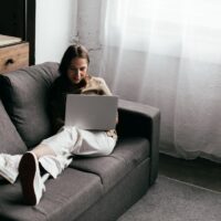 Selective focus of young woman with prosthetic leg using laptop on sofa at home