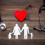Take out health insurance for family. Stethoscope, paper heart and silhouette of family on wooden background top view Take out health insurance for family. Stethoscope, paper heart and silhouette of family on wooden background top view
