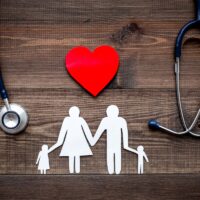 Take out health insurance for family. Stethoscope, paper heart and silhouette of family on wooden background top view