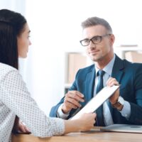 insurance agent pointing at clipboard in clients hand at tabletop in office, house insurance concept