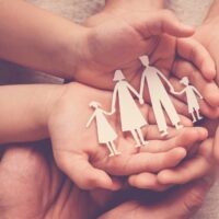 Adult and children hands holding paper family cutout, family hom Adult and children hands holding paper family cutout, family hom