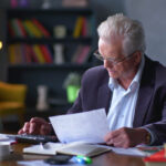 Senior man with papers or bills counting on calculator at home